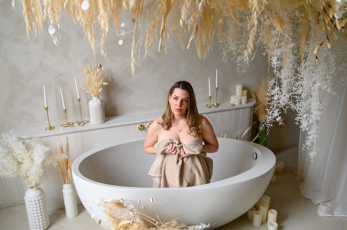 Blonde woman sitting in a bathtub with a beige towel