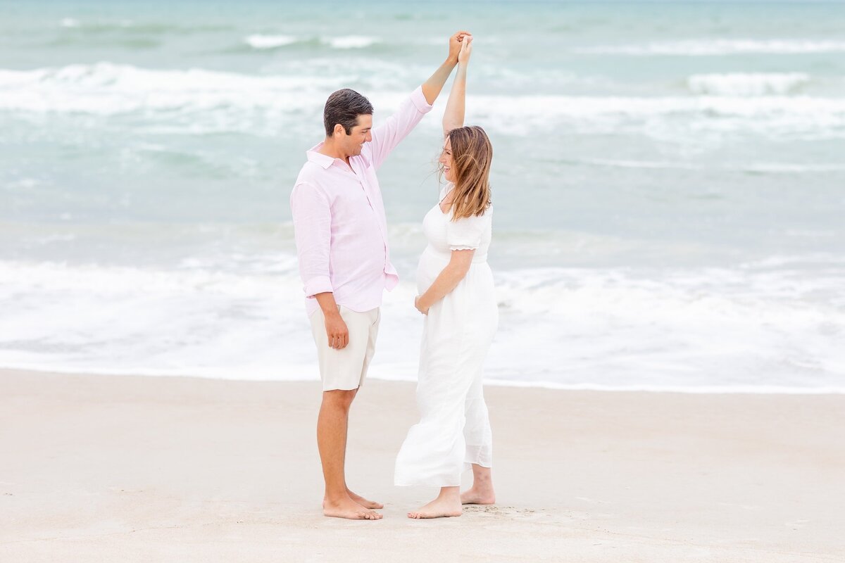 Maternity couple dances in front of the ocean