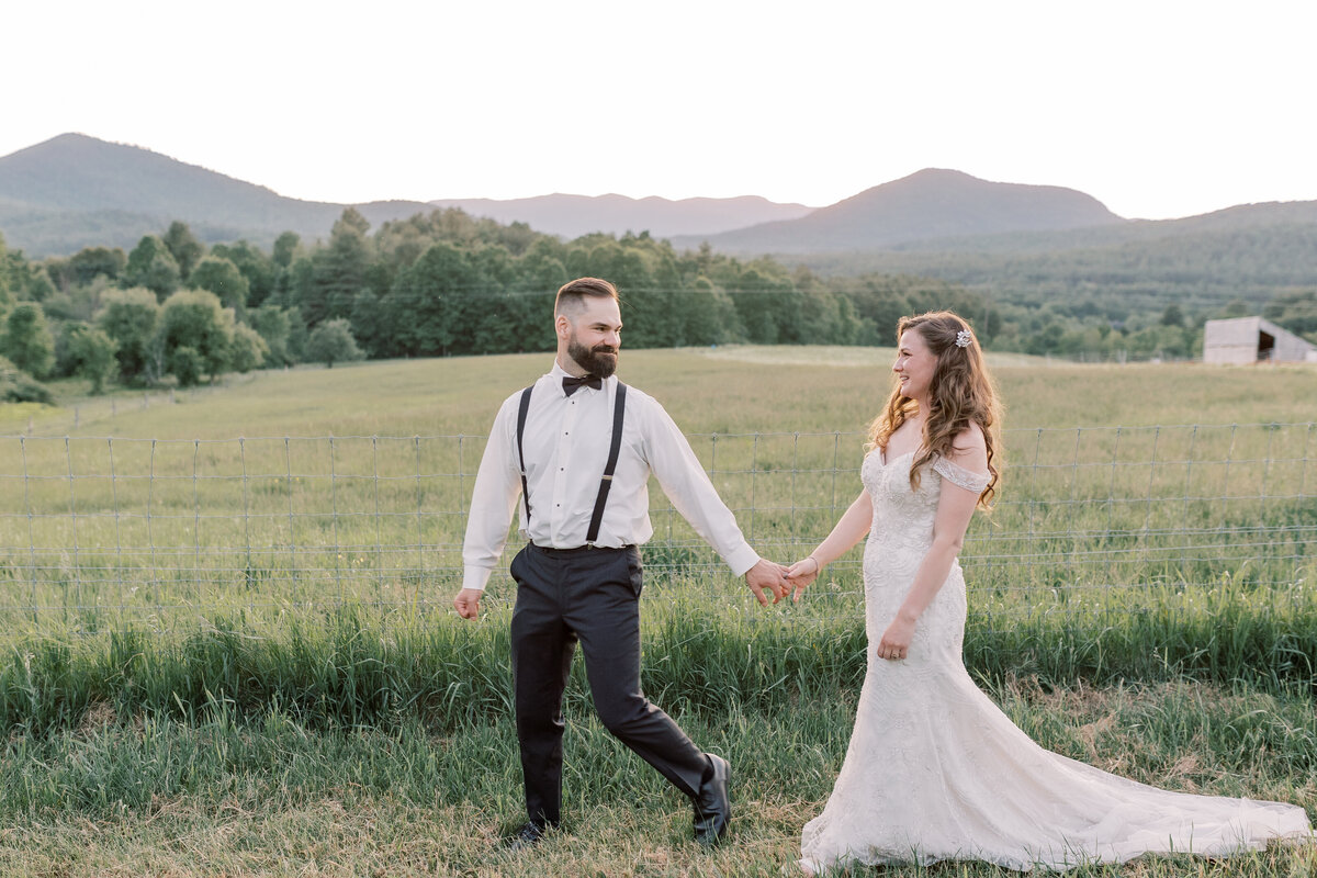 Couple walking through a field with the Adirondack mountains in the background during their elopement near Lake Placid.