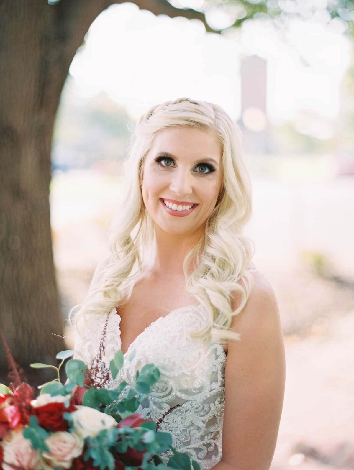 Blonde bride in a white wedding gown smiles at the camera while holding a floral bouquet with orchids and roses
