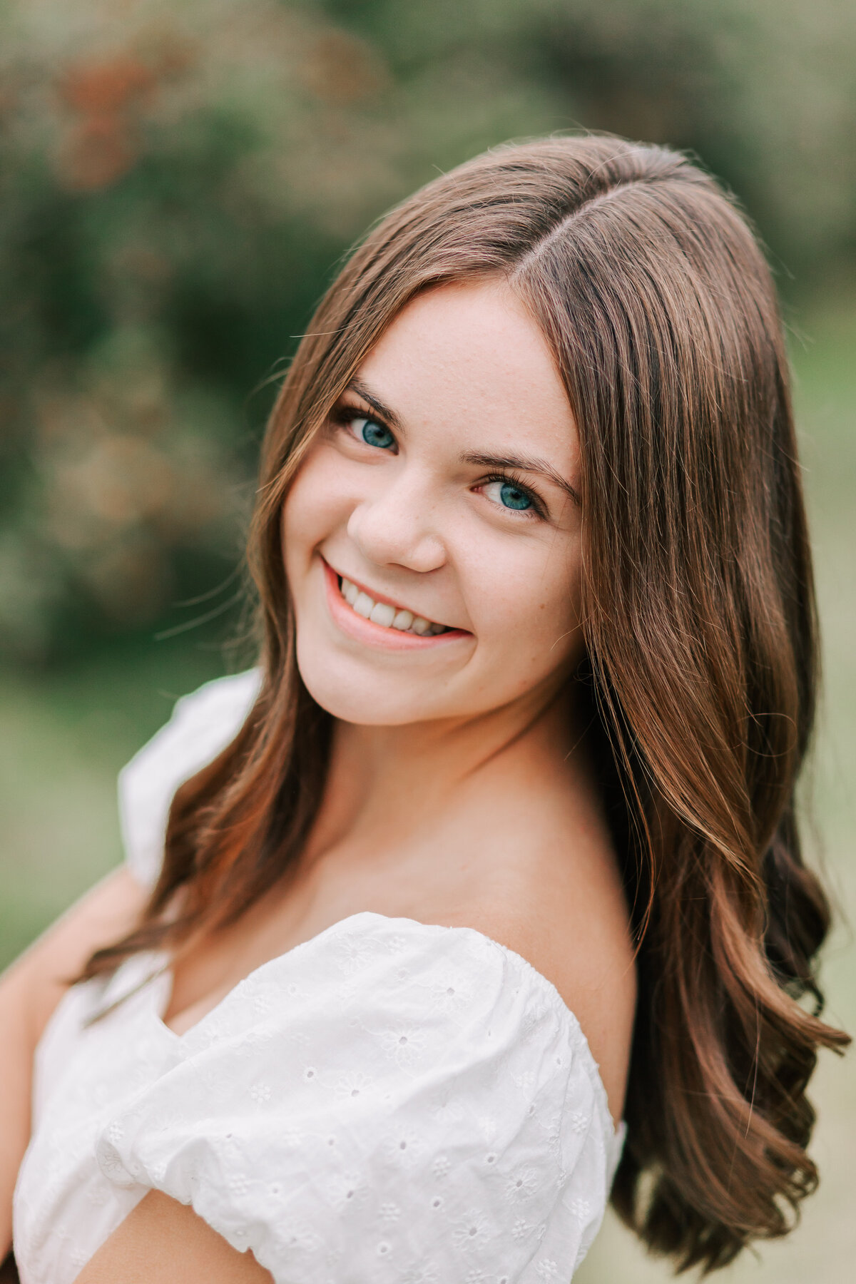 A senior girl leans toward the camera smiling. Photo by Jen White Photography