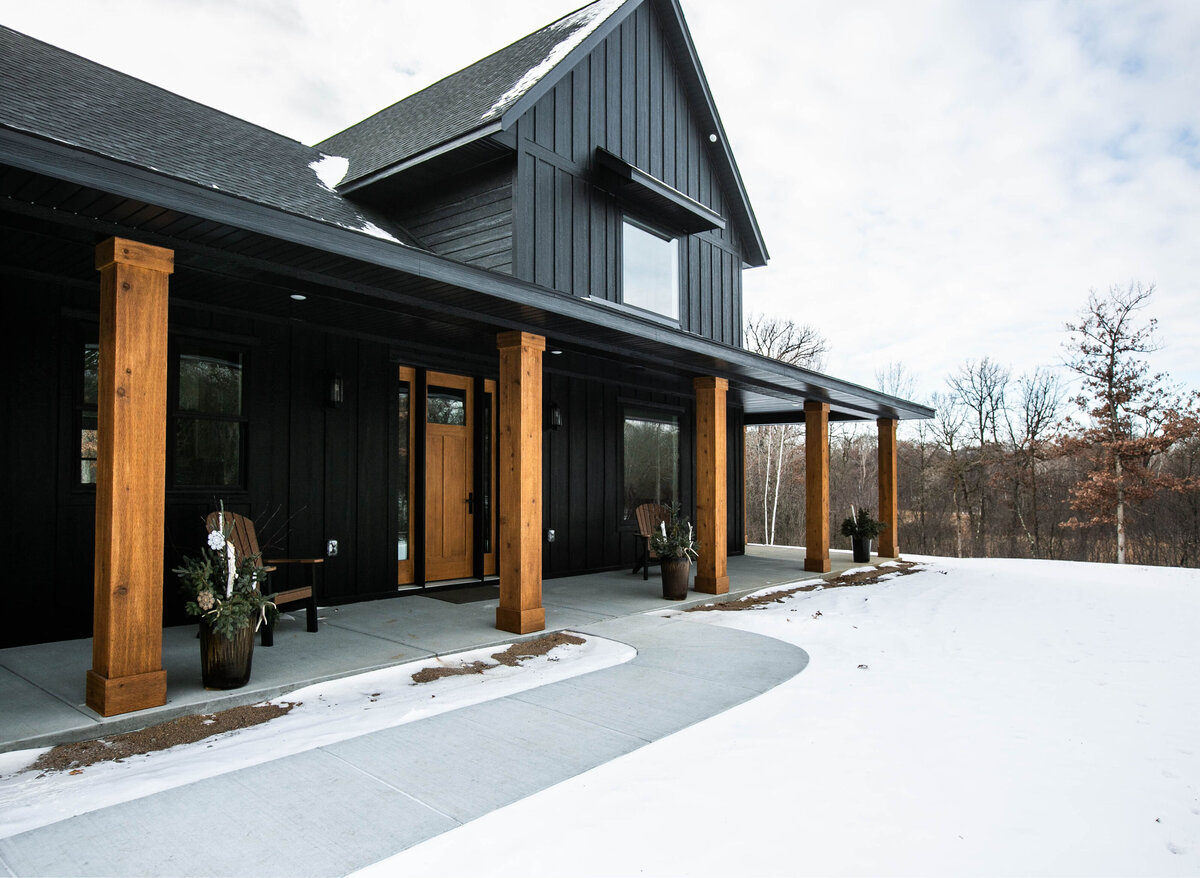 Exterior view of custom home in Elk River, Minnesota with black siding, wood details and front porch built by Cornerstone Custom Builds