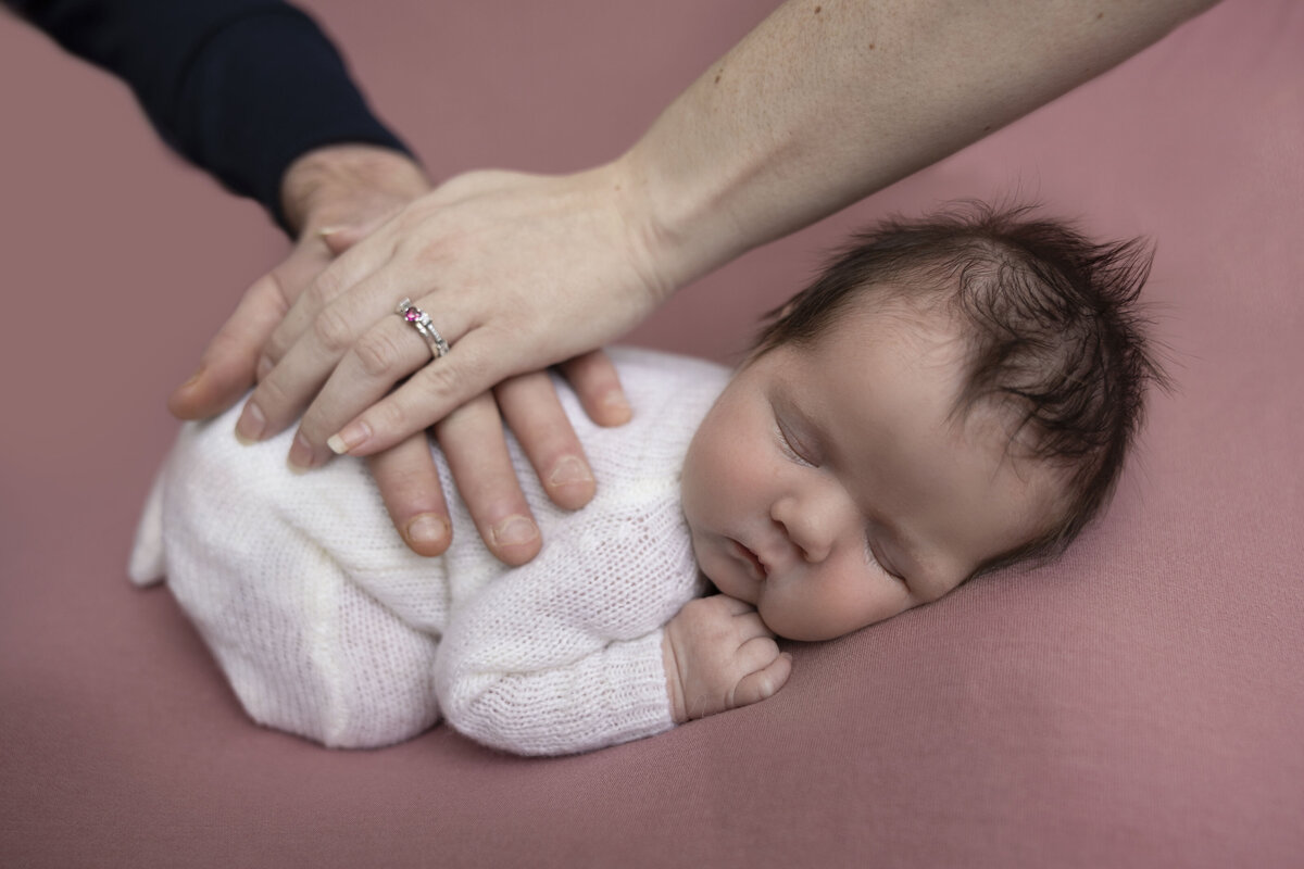 Mom and dads hands lay on top of their newborn baby girl.