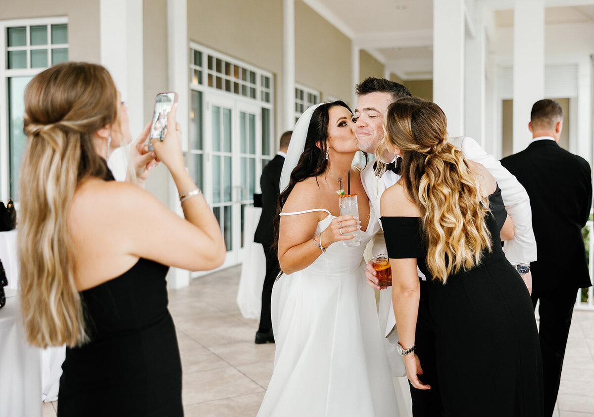A candid moment of the bride kissing the groom, surrounded by laughter and joy during Ashley and Cameron's micro wedding reception at Ocean Reef in Key Largo, captured by Claudia Amalia Photography.