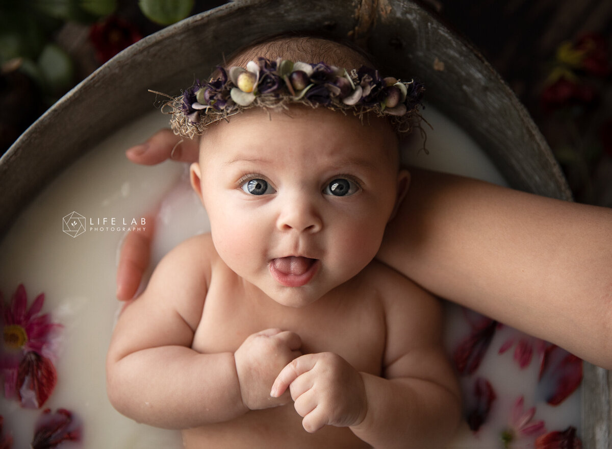 baby girl with big eyes looking at the camera in her milkbath