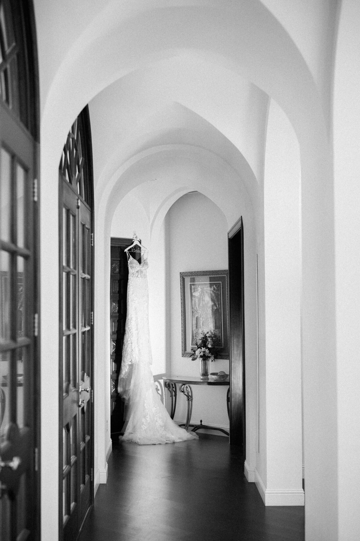 Elegant lace wedding dress hanging in an arched hallway at White Swan Castle in Granite Bay, California, before the ceremony.