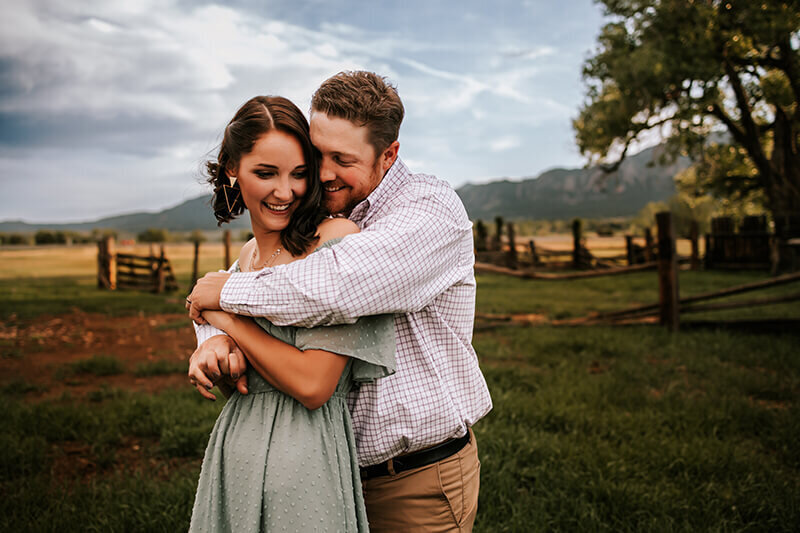 Husband hugs wife from behind in a grassy field in Boulder, Colorado