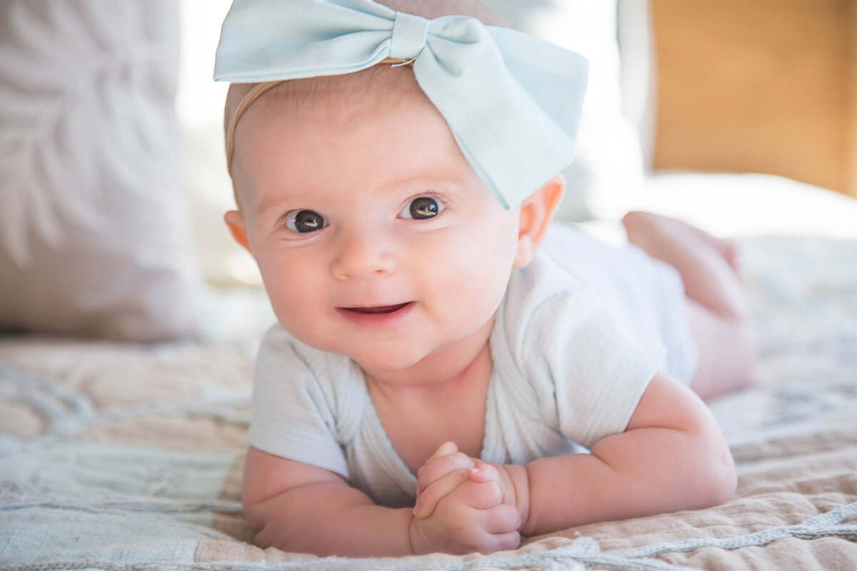 infant girl doing tummy time happily on a bed during session with las vegas milestone photographer