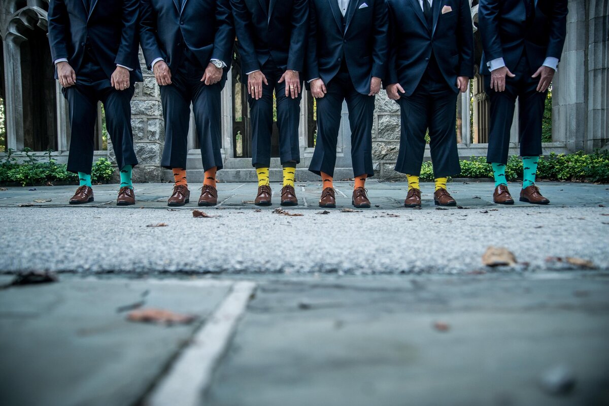 a group of groomsmen hold up their pants, showing off colorful socks