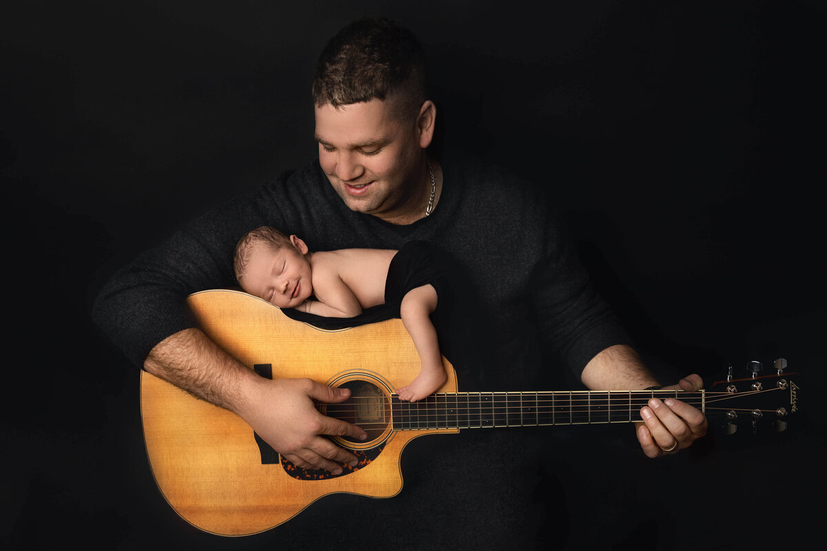 Newborn boy sleeping on dad's guitar and smiling