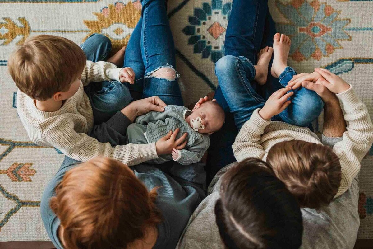 Family gathers together around their sleeping newborn on a vibrant patterned rug during an intimate lifestyle photography session.
