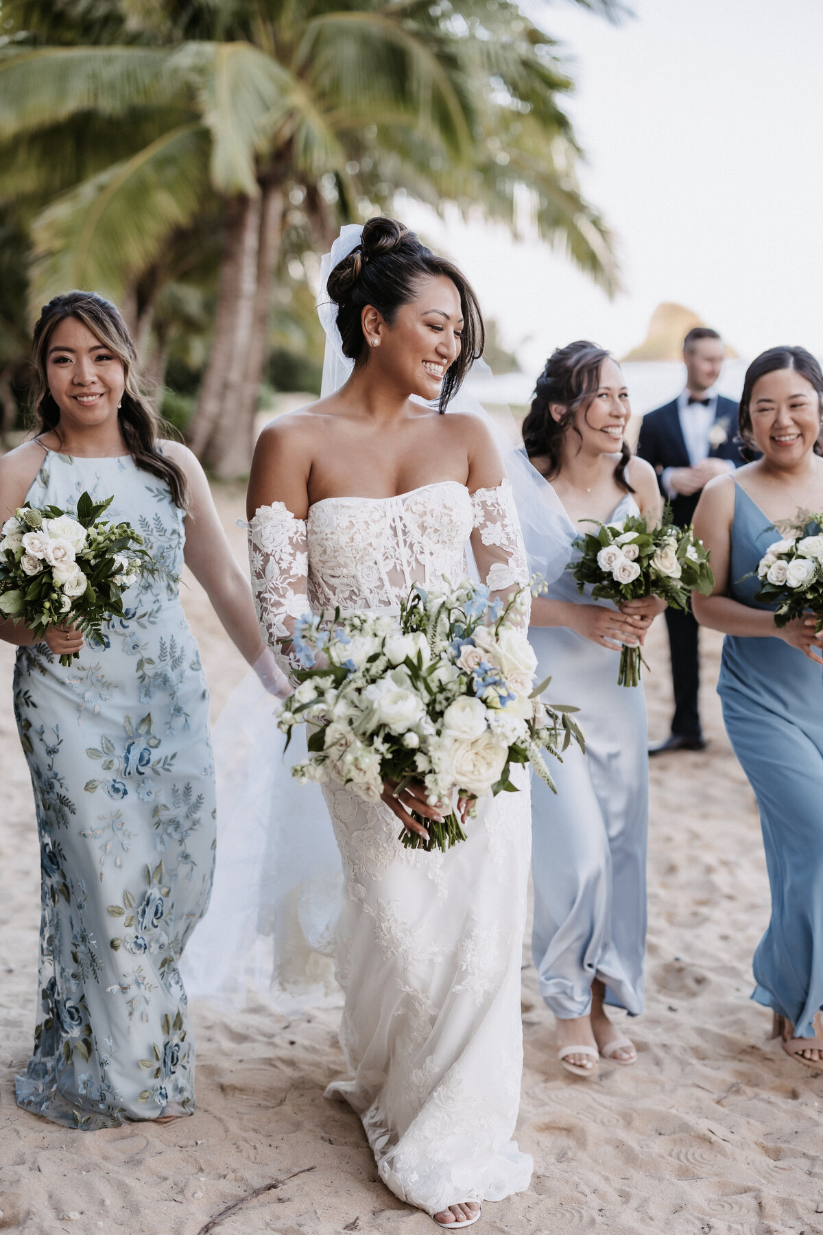 Bridesmaid and bridesman portraits wearing shades of blue holding bouquets on the beach with palm trees behind