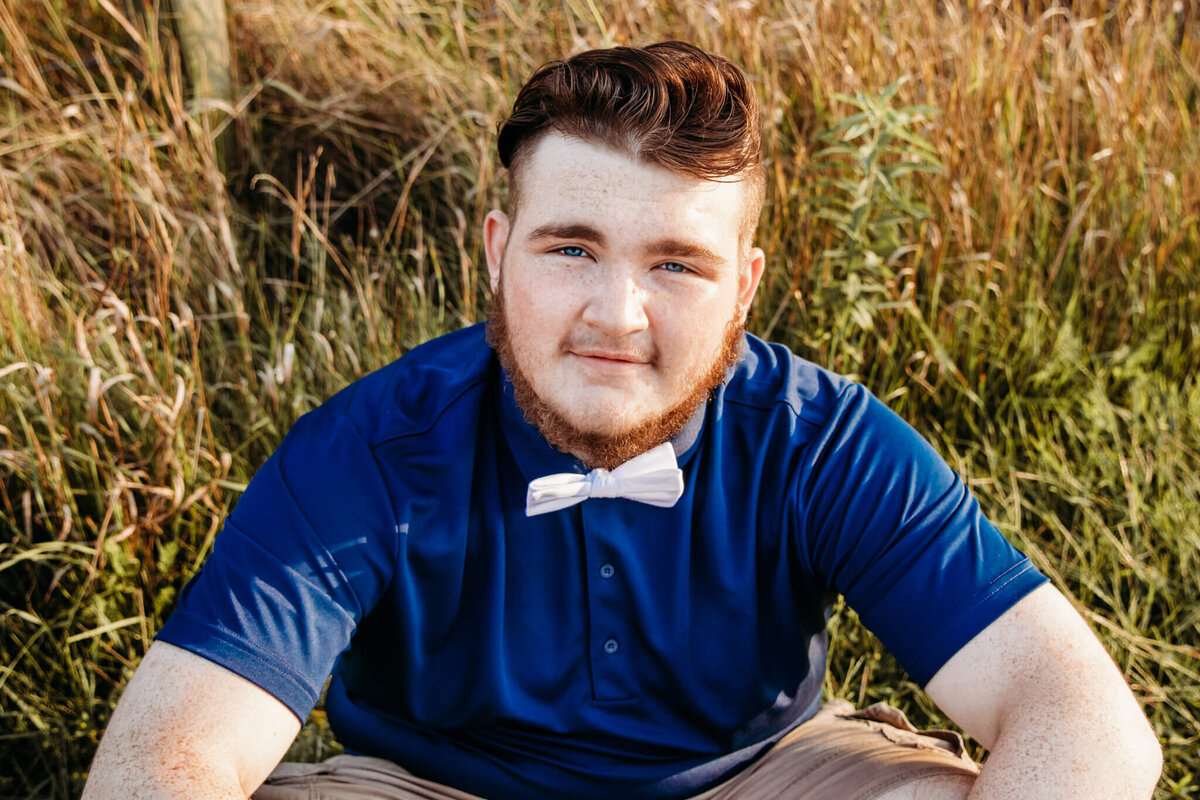 high school senior boy  wearing a white bow tie sitting in tall grass