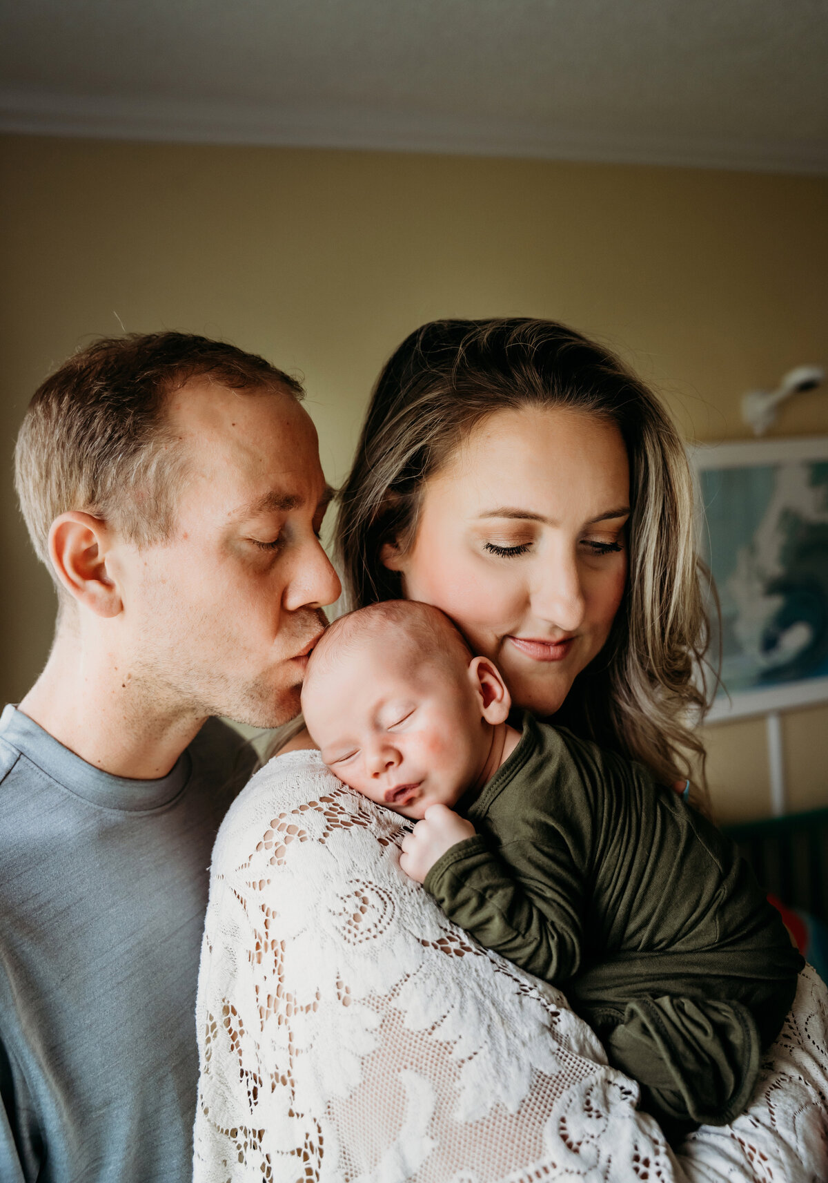 Newborn Photography, a mother holds baby as dad leans in from behind to give him a kiss