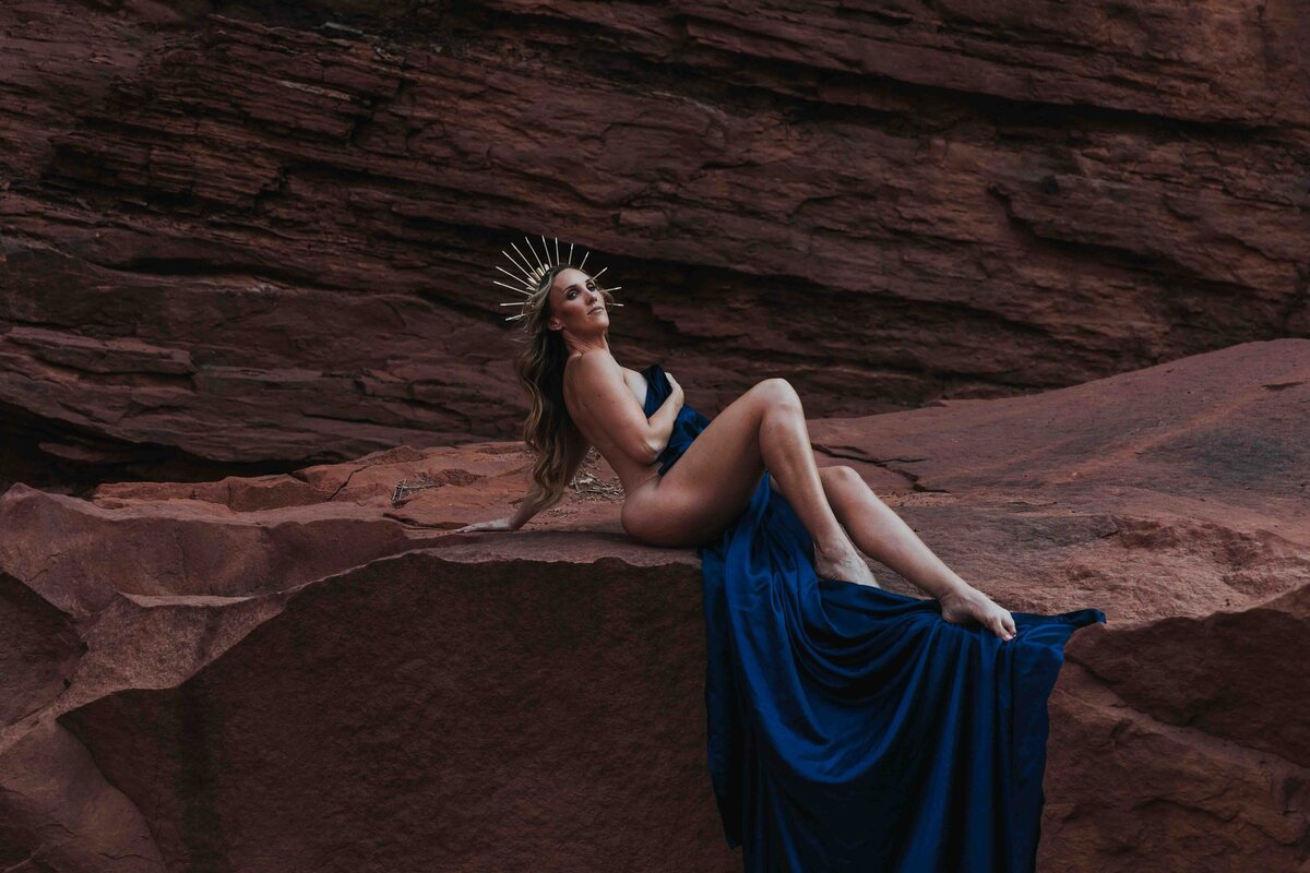 A woman laying on a massive boulder wearing only a sheet and a crown.