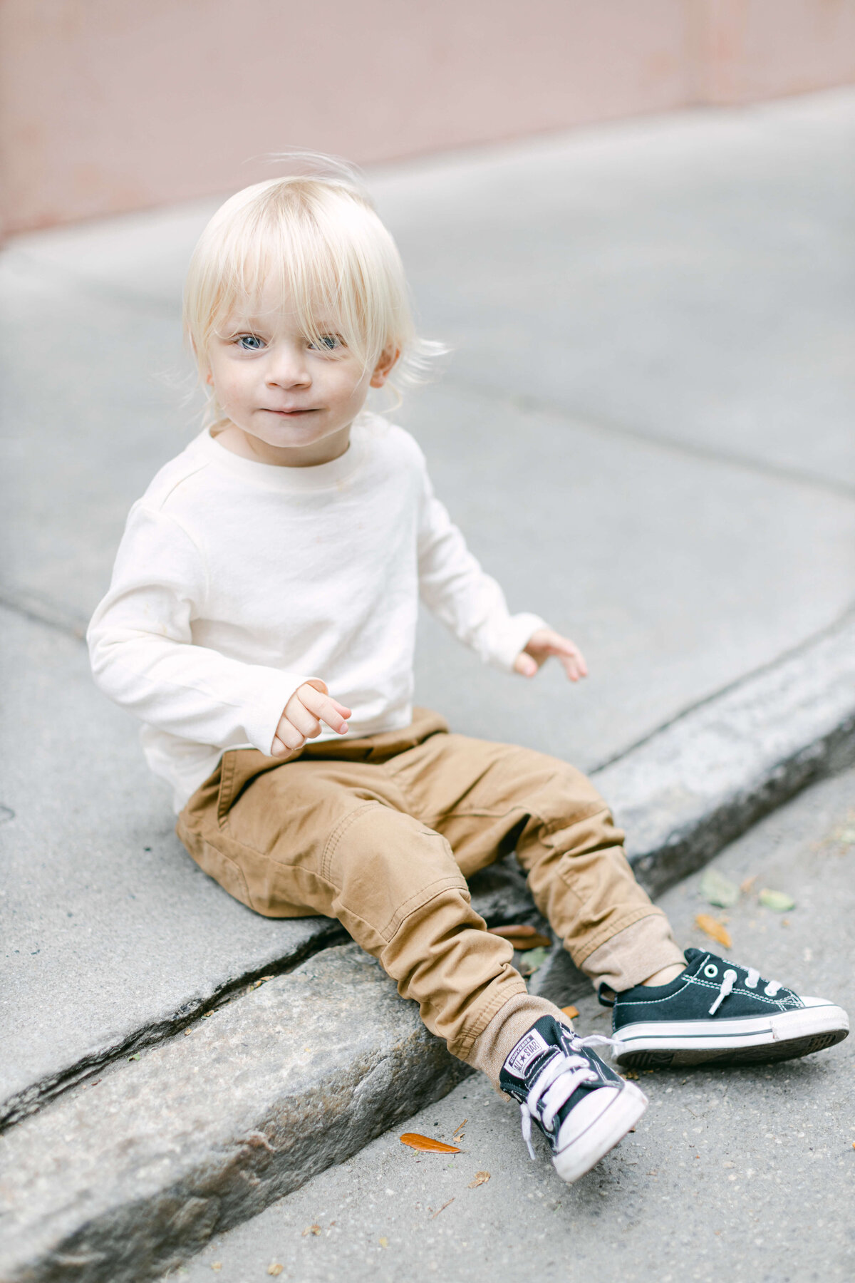 A small blonde child with blue eyes sits on a curb.
