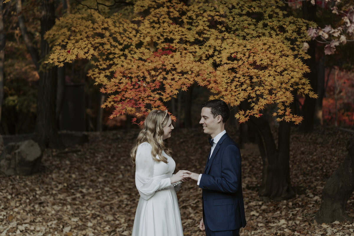 the bride putting the wedding ring to the groom while standing outside in autumn leaves