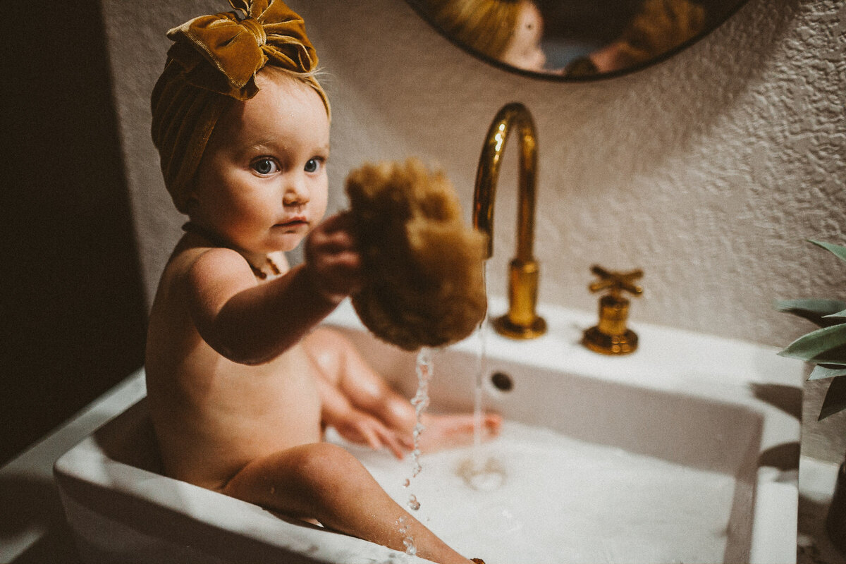 baby takes a sponge bath in the sink in her family bathroom