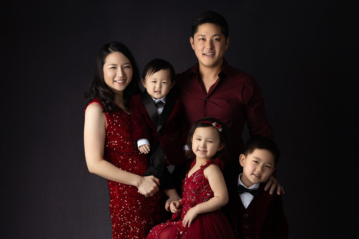 Dallas baby milestone photographer captures a joyous family in rich red attire, radiating love and elegance with matching outfits and smiles.
