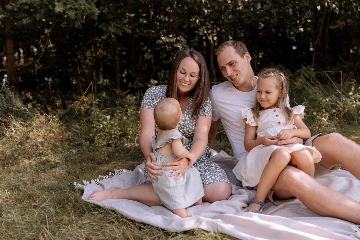 Eine Familie bestehend aus Vater Mutter und zwei Kindern sitzt auf einer Decke auf einer Wiese