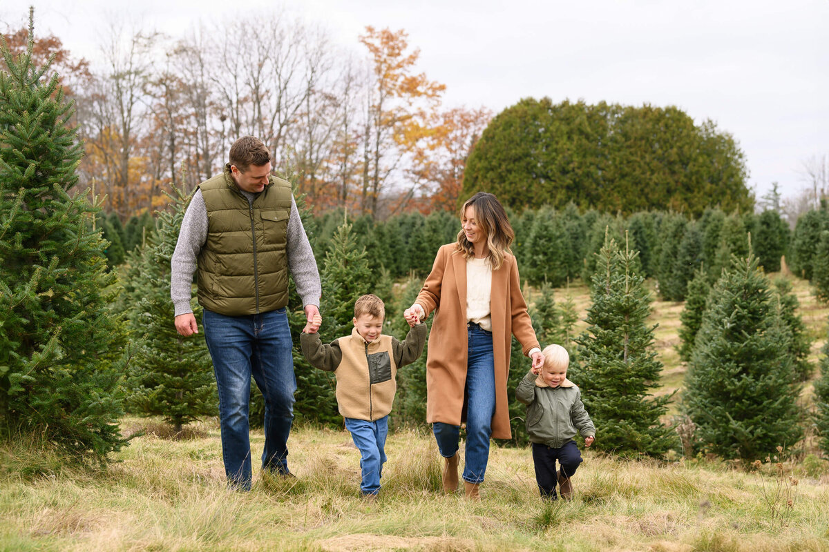 Mom and dad holding their boys hands walking in a Christmas tree farm for their family photography session Burlington, On
