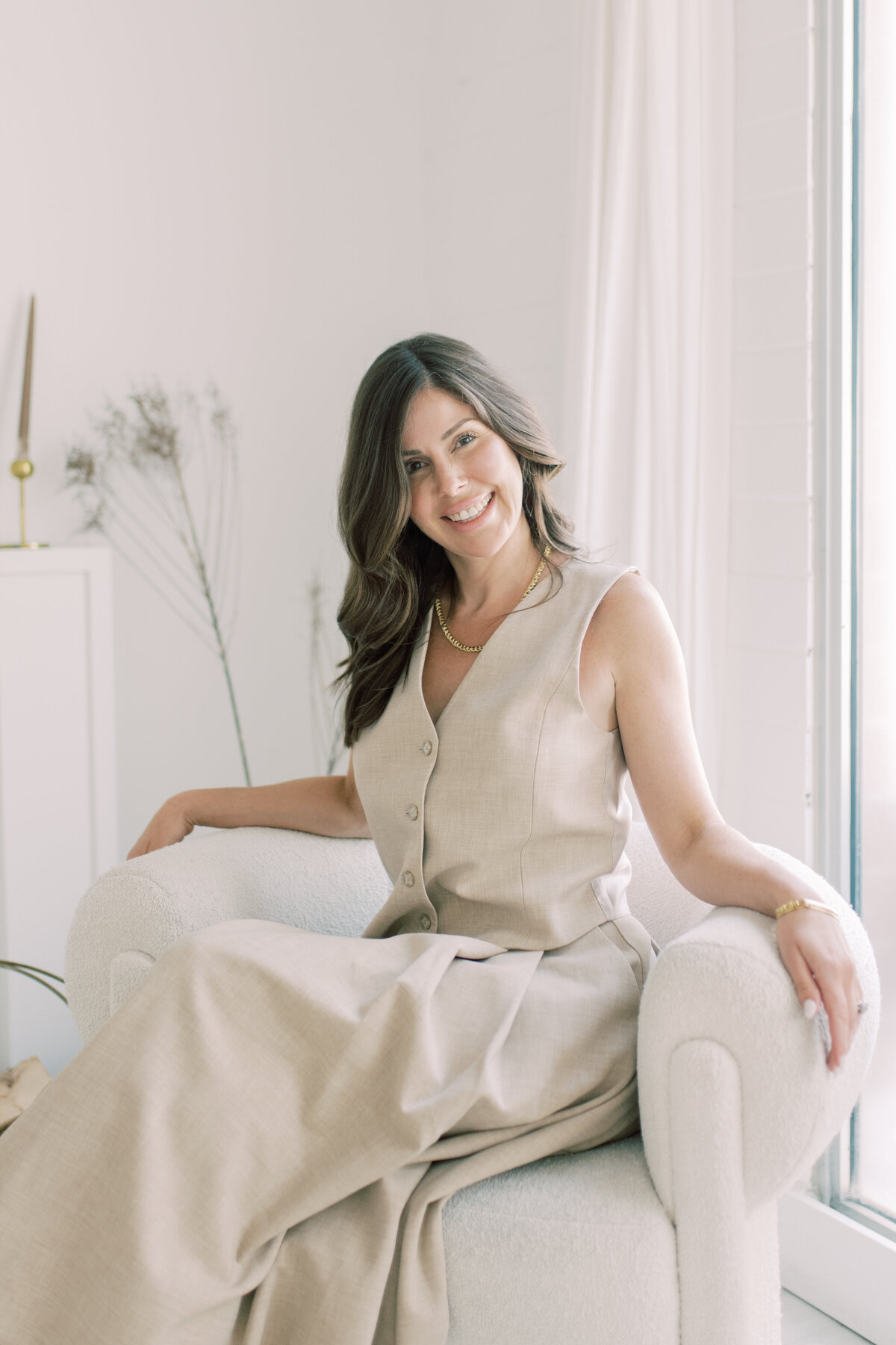 Brunette woman in linen vest and skirt, smiling softly in natural light—cosmetic expert portrait
