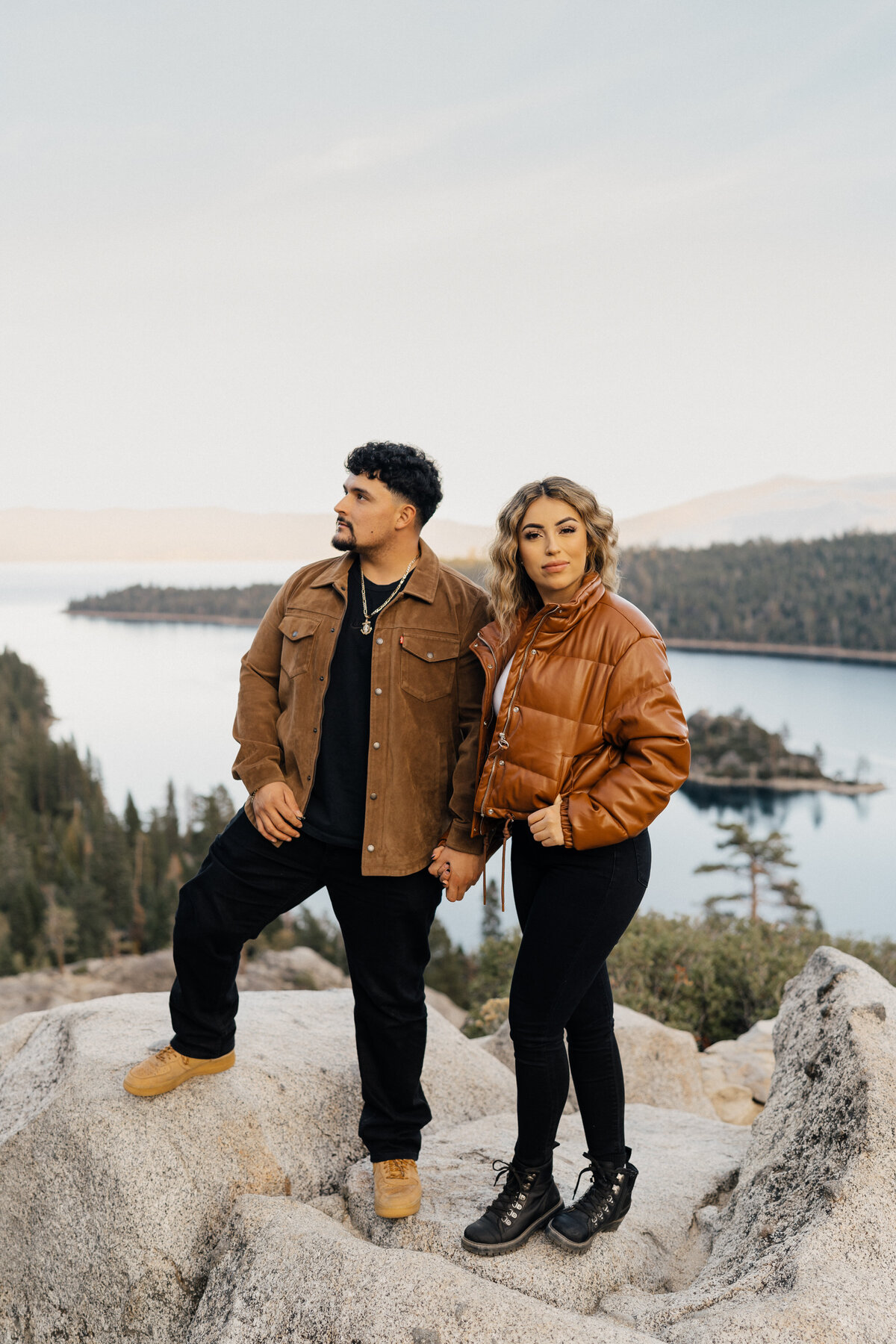 A couple embraces on the shore of Lake Tahoe during their engagement session, surrounded by stunning mountain views.