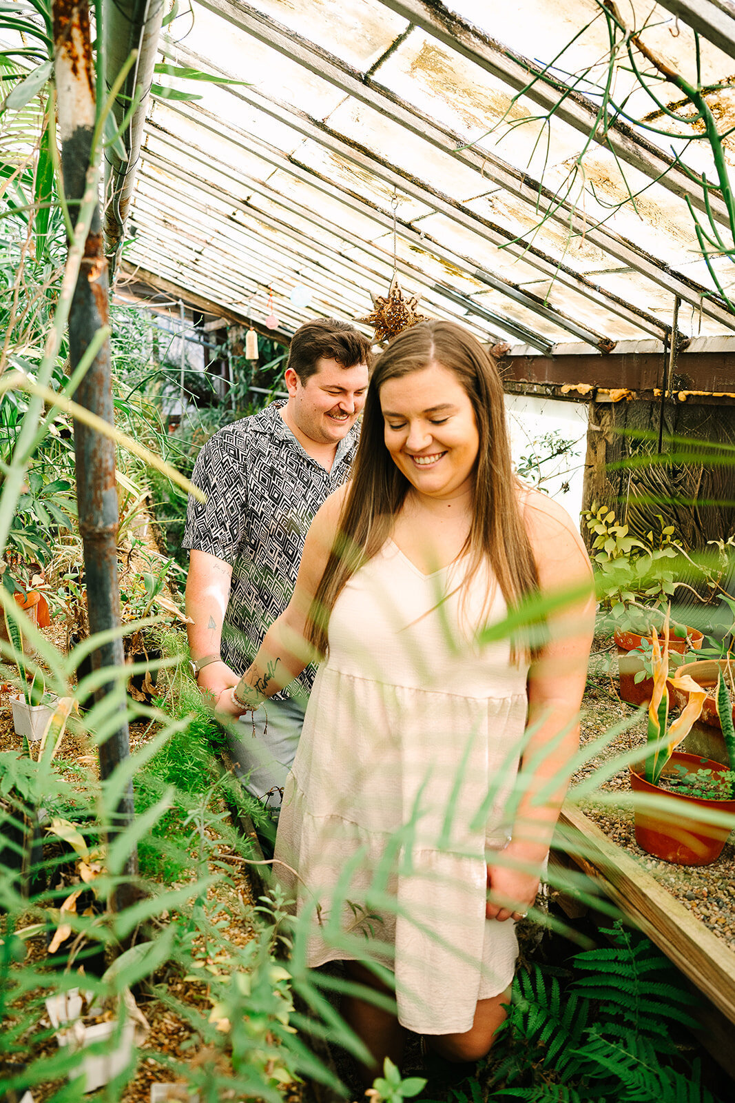 A couple holding hands and smiling while walking through a greenhouse 