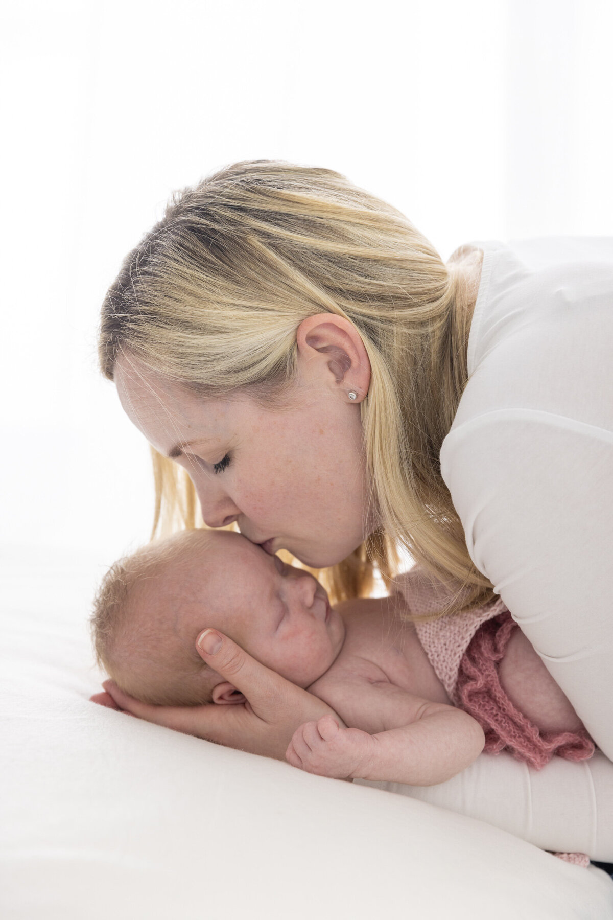Fotografert i profil; mor kysser babyen sin som ligger i armene hennes på et teppe. Fotografert i Studio Landmark, Fyllingsdalen.