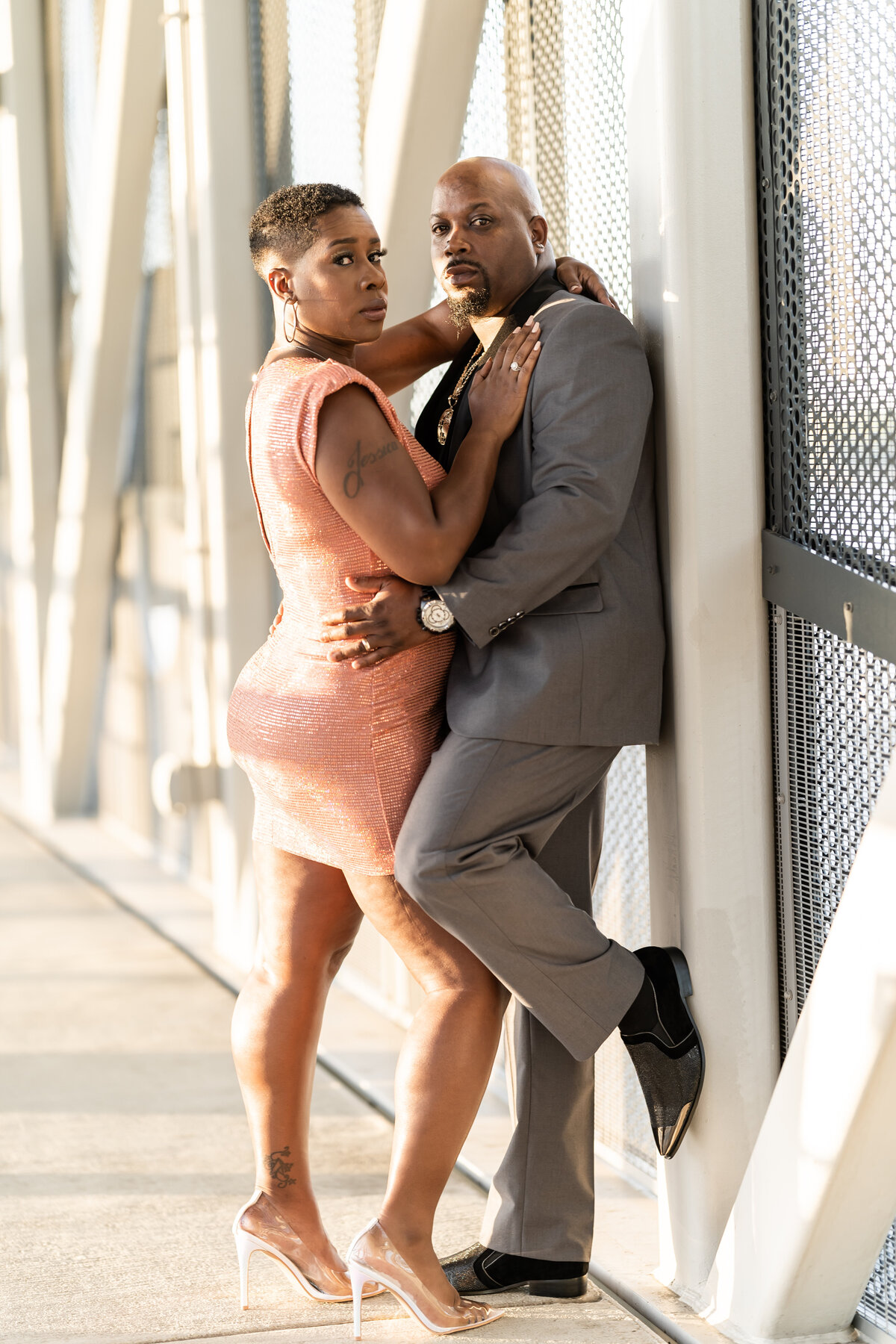 Wedding anniversary photoshoot couple on bridge man wearing grey suit, woman wearing coral sequin dress