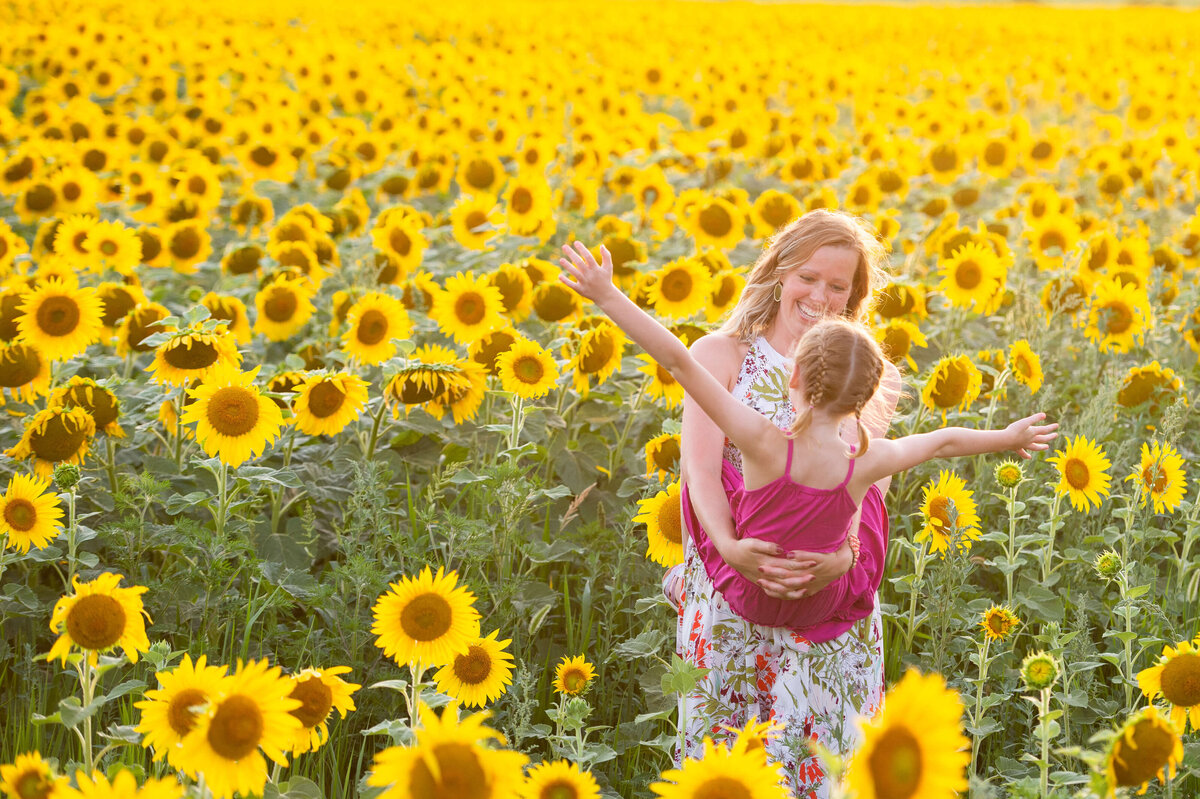 mom and daughter laughing and playing in a sunflower field at sunset captured by Ottawa Family Photographer JEMMAN Photography