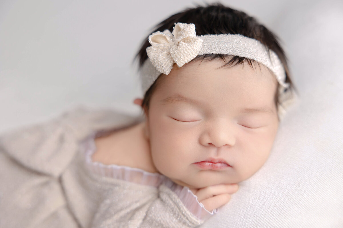 Newborn baby girl wearing a organic cream headband and a sparkling dress while lying soundly asleep at Heather Nicole Photography