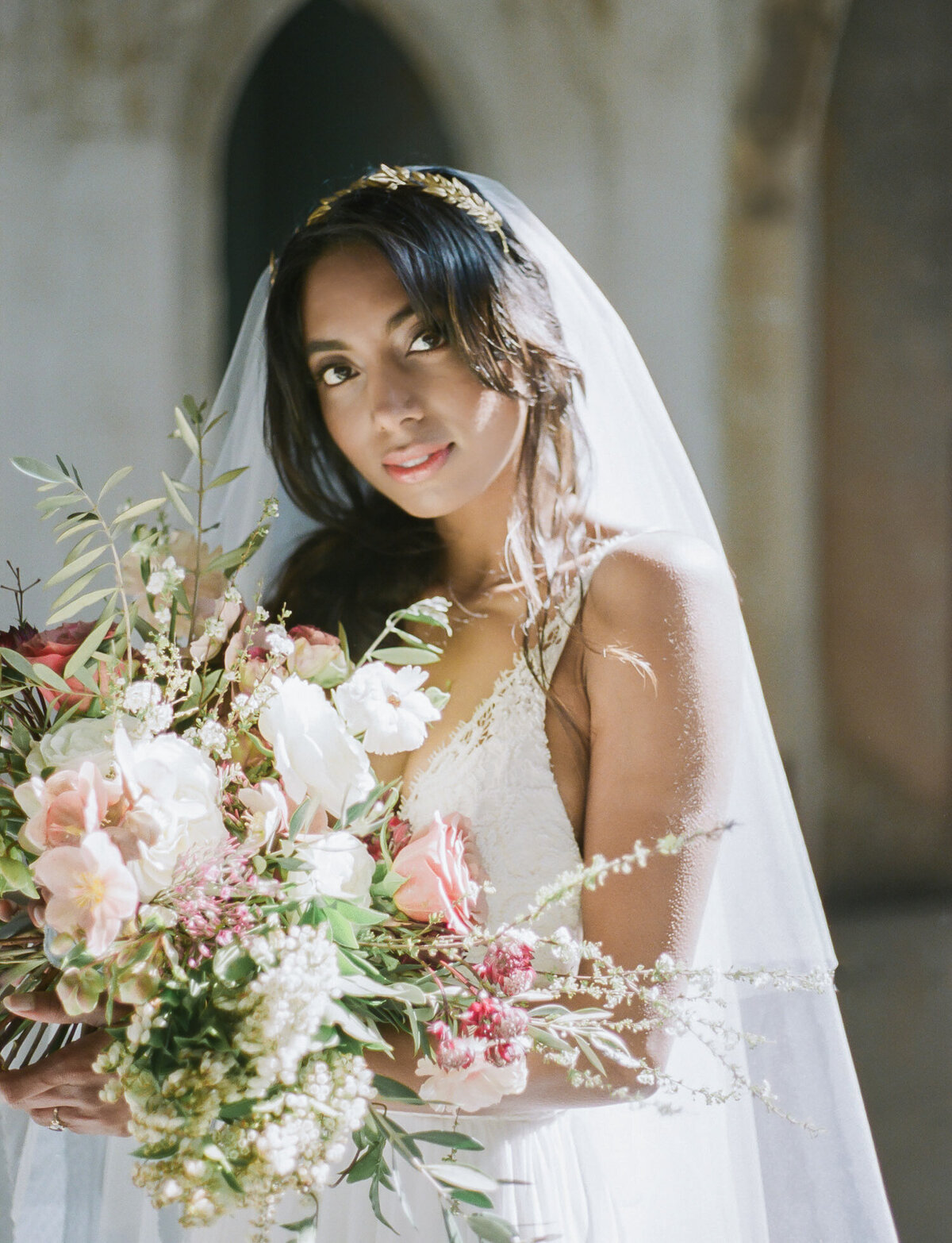 Indian bride holds colorful bouquet in ruins wedding venue, abandoned cathedral wedding in Italy