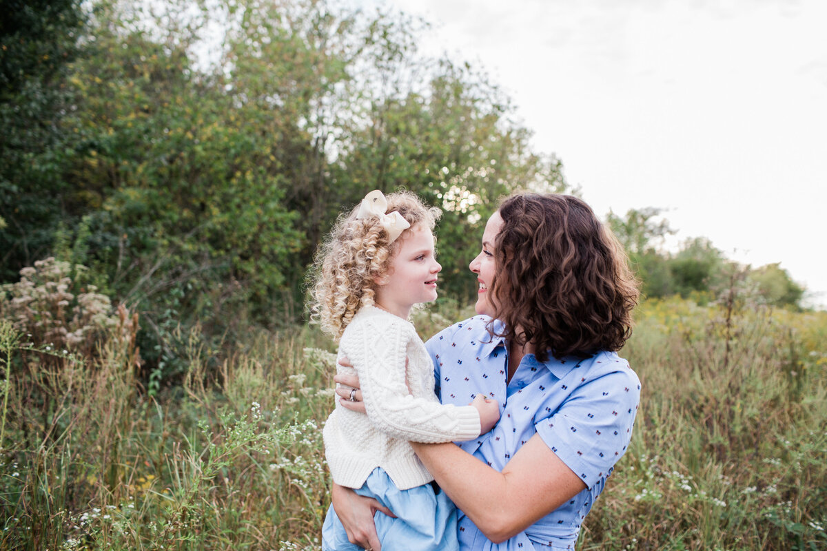 mom holding her daughter at fall family session in a field