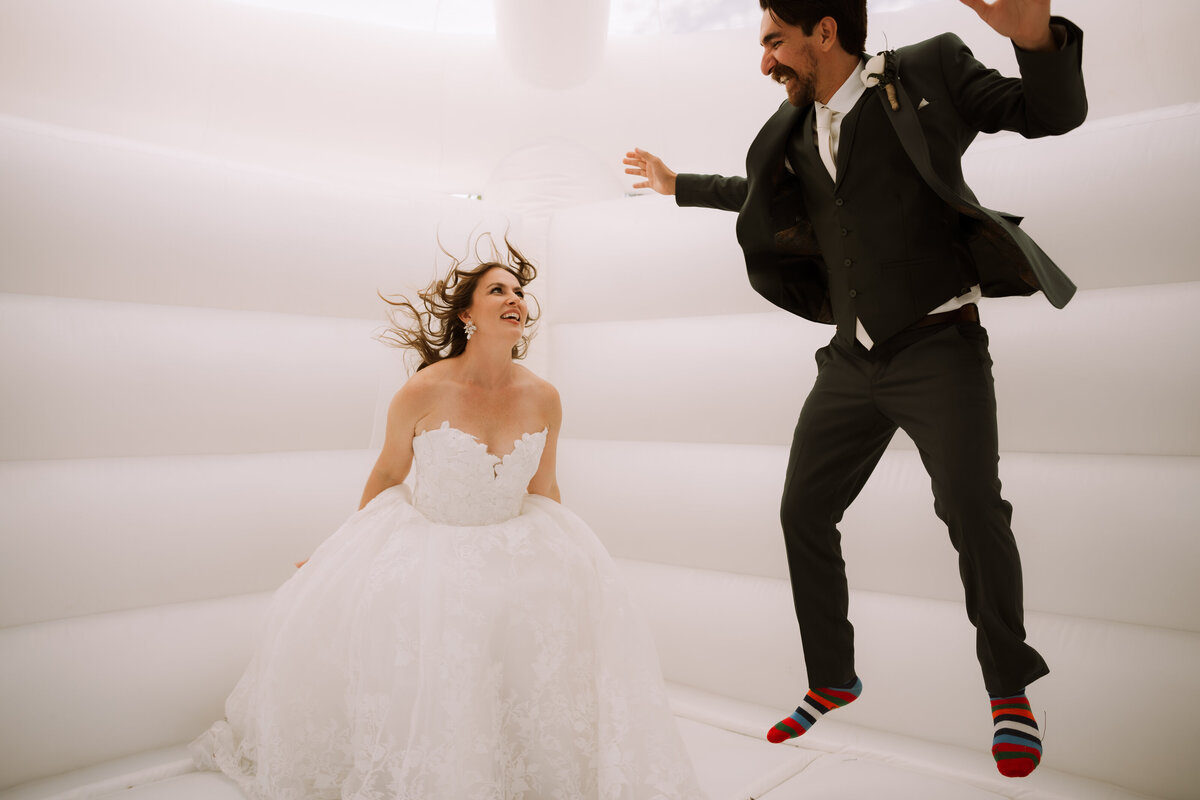 bride and groom jumping in white bouncy house at their wedding