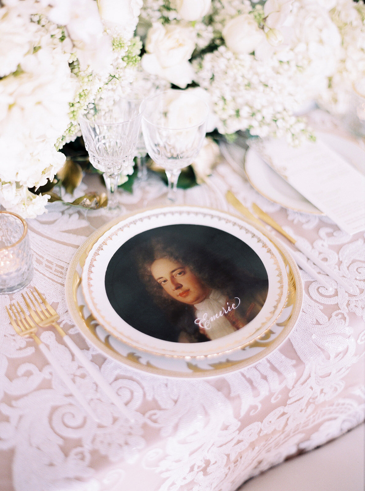 The photo at Chateau Vaux le Vicomte, one of the top destination wedding venues in France, was taken by photographer Audrey FORA. In addition to the photographer, East West Films Videographers also captured the beautiful scene. The stunning table setting features elegant white and gold dinnerware, with a portrait plate depicting a historical figure and the name Emrick delicately written on it. Adorned with white flowers, sparkling crystal glasses, shining gold cutlery, and a delicate lacy tablecloth, the setting offers a truly exquisite ambiance.