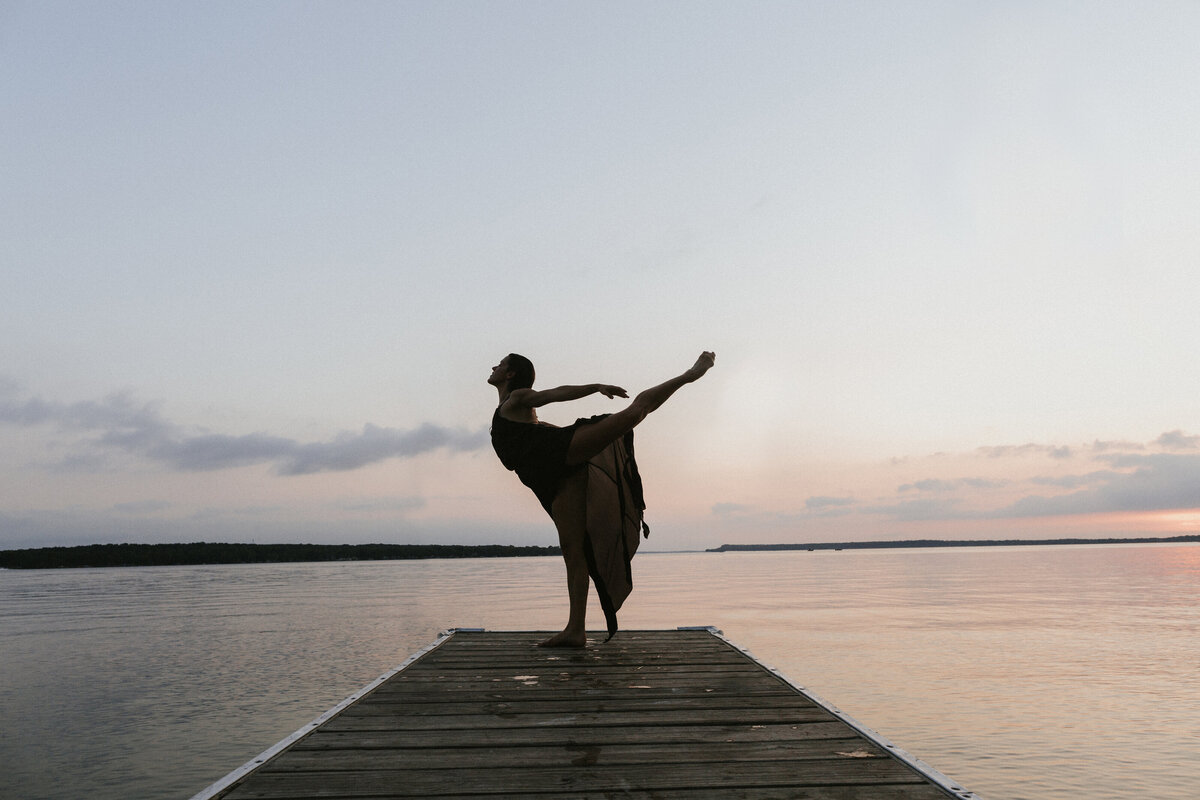 Woman dances on dock on lake at dusk
