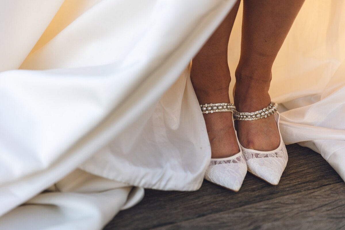 Close-up of bride's pearl-embellished shoes and wedding dress train