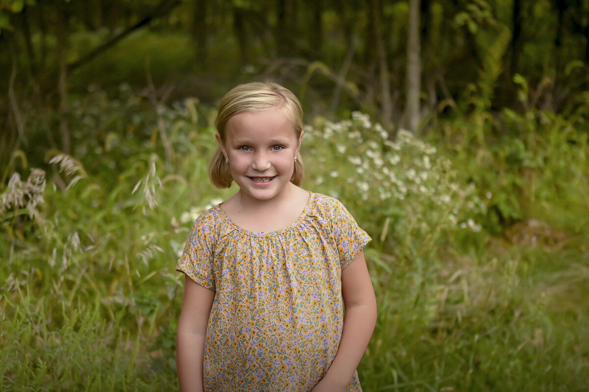 A young blonde girl wearing a floral top smiles