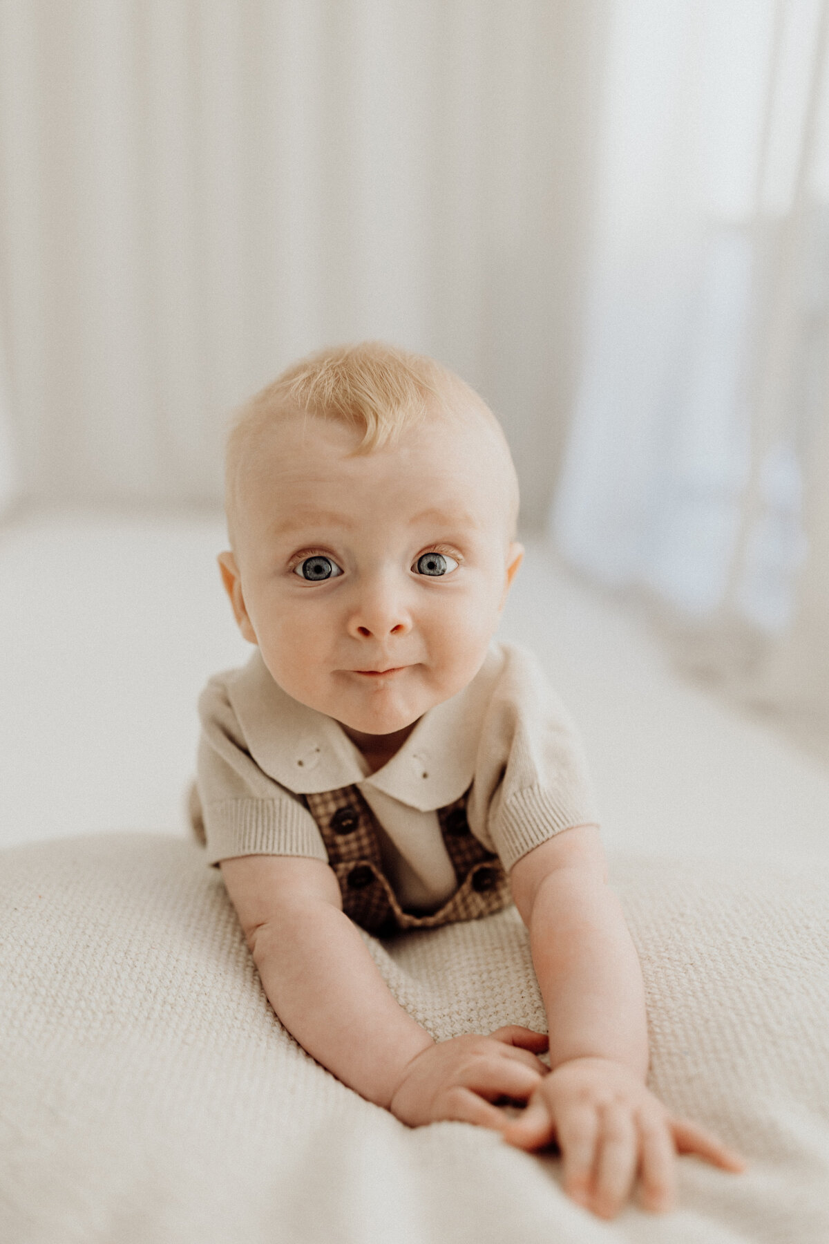A little baby boy leans on a white prop while the sun shines through the window behind him in the photography studio of lucy jane, a top photographer in christchurch