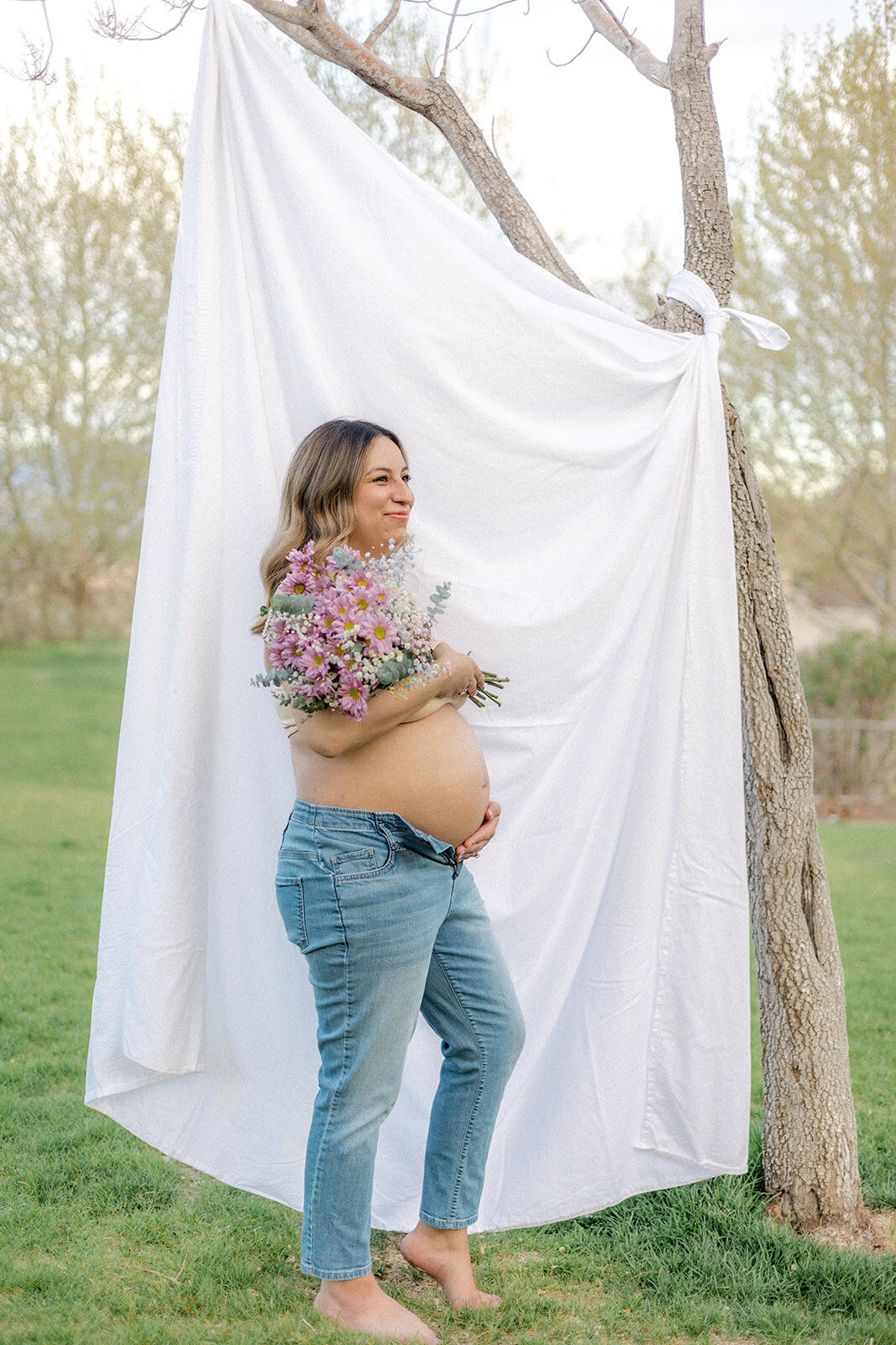 A pregnant woman holds her belly while holding flowers