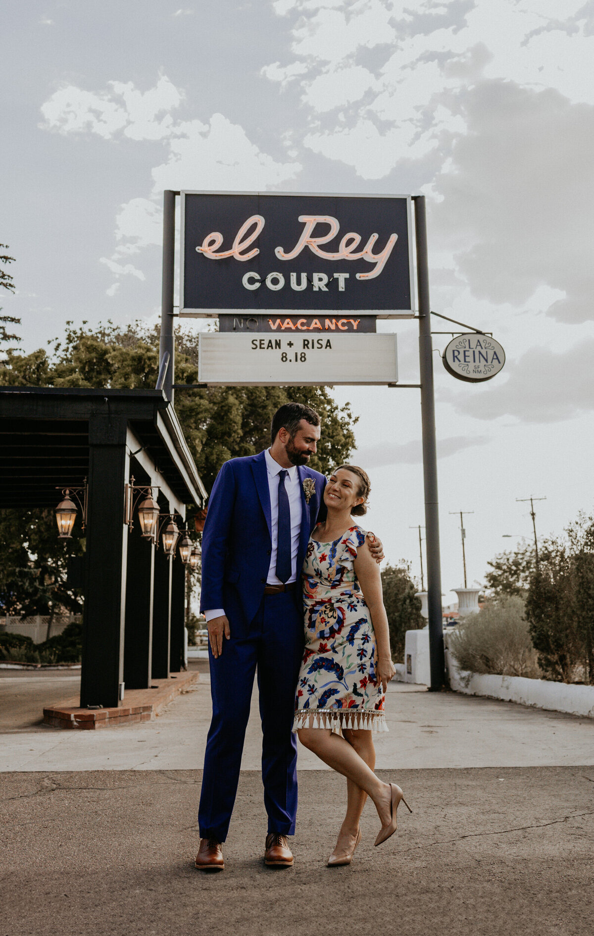 bride and groom stand in front of El Rey Court sign in Santa Fe featuring their names and wedding date