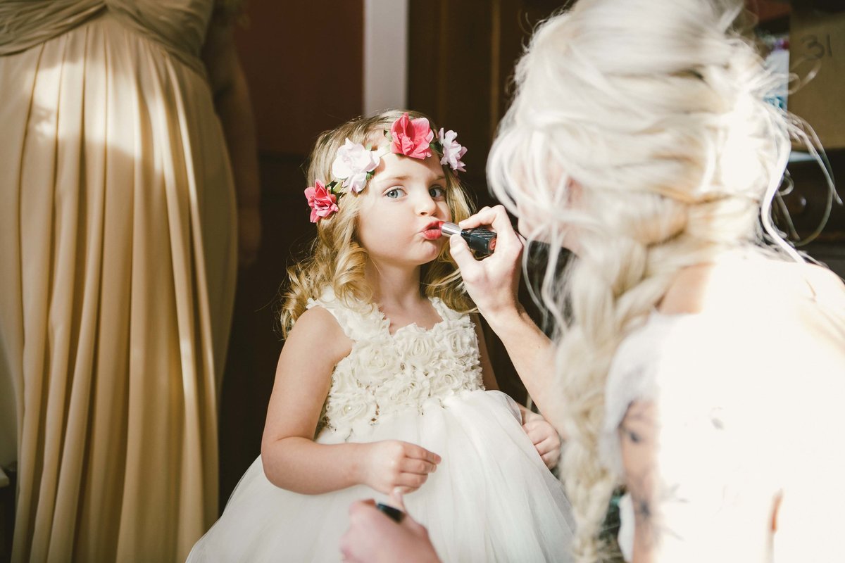 Flower girl puts on lipstick held by bride at Mustard seed garden wedding