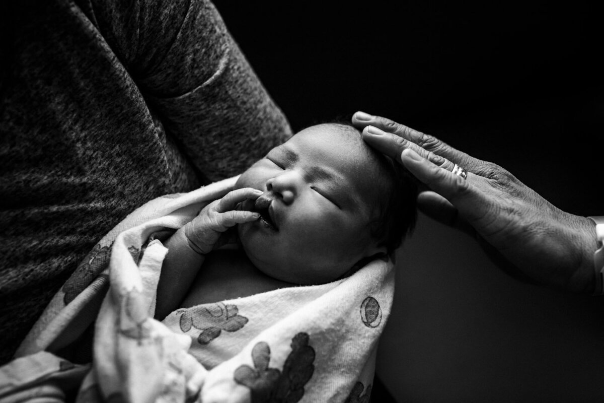 newborn swaddled and sleeping with dad touching her head