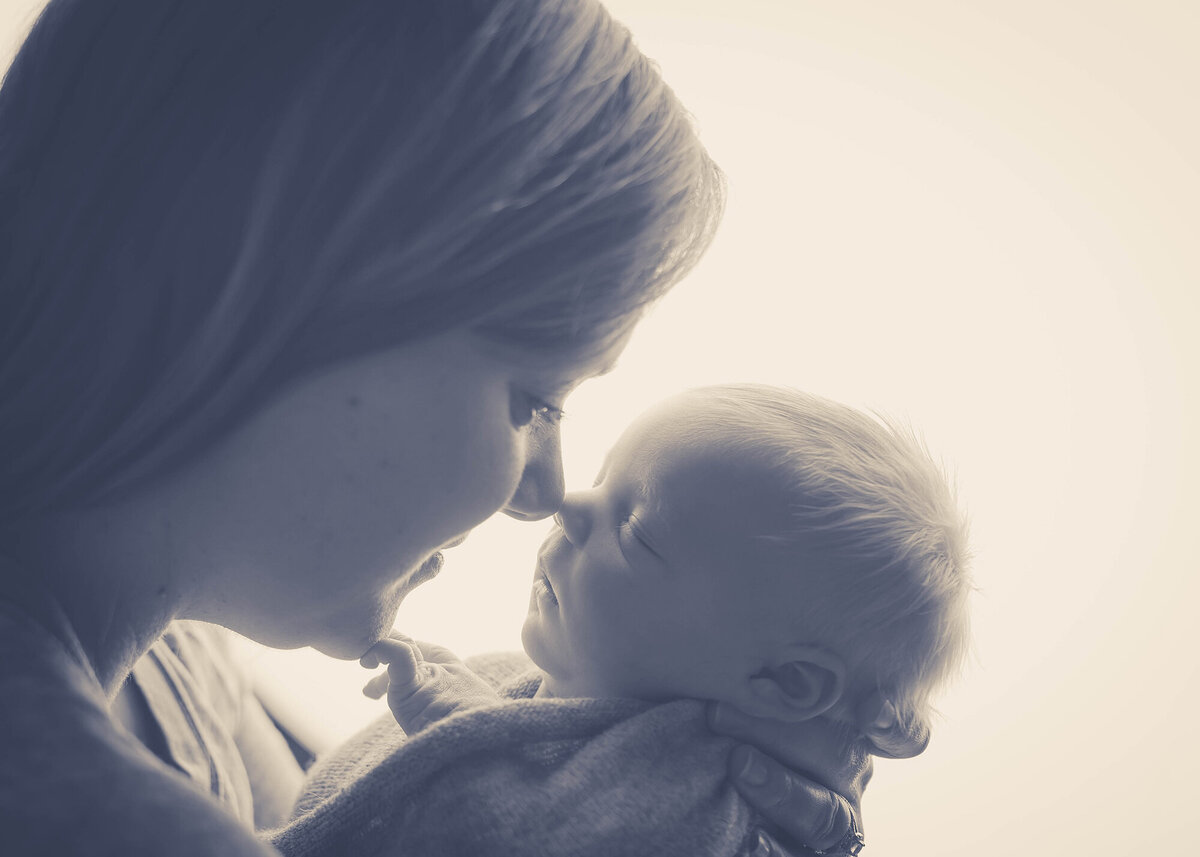 A new mom boops noses with her newborn in her hands for an Iowa Newborn Photographer