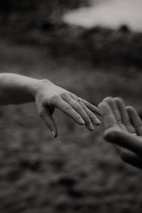 Main de la mariée tendue vers la main de son partenaire, mettant en valeur son alliance. Photographie en noir et blanc par Kamescop, photographe vidéaste de mariage en Bretagne.