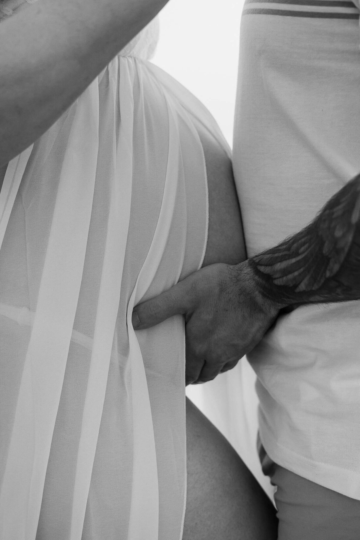 A black and white photo of dad cradling mom's pregnant belly during Cleveland beach maternity photography session.