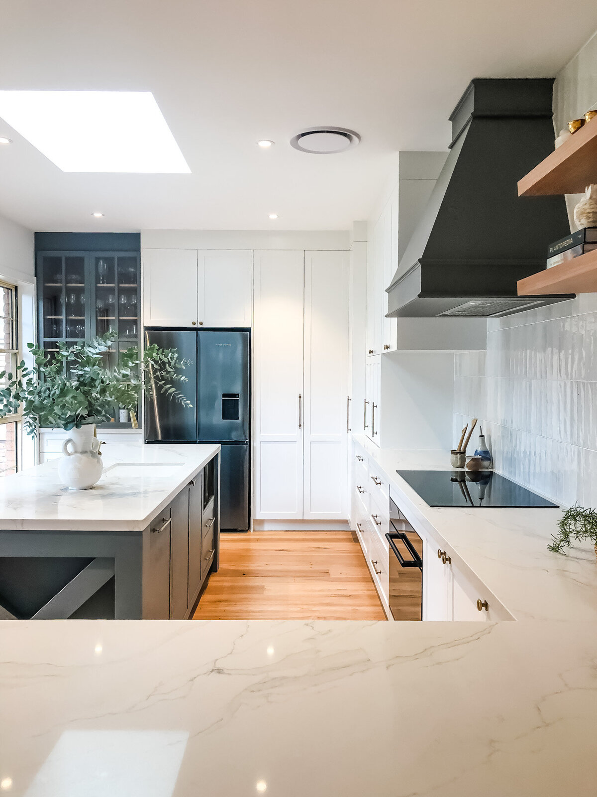 Experience a luxury home design in this modern kitchen featuring white cabinets, a sleek black range hood, and an island adorned with plants. The elegant wood flooring ties the space together in a showcase of bespoke interior design Newcastle NSW prides itself on.