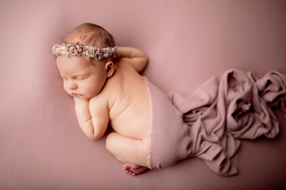 Overhead newborn portrait of baby in pink with pink fabric flowing behind her 