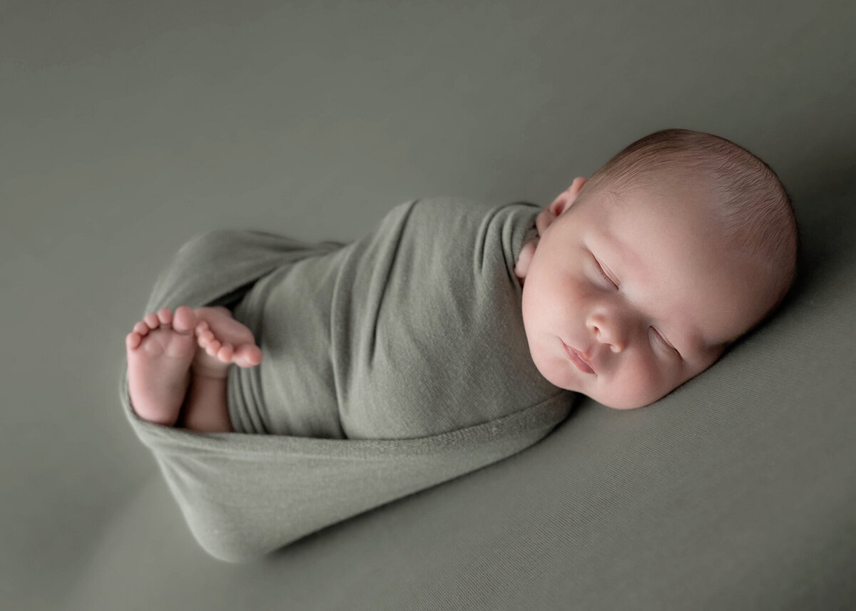 A newborn baby sleeping in a green swaddle with feet poking out
